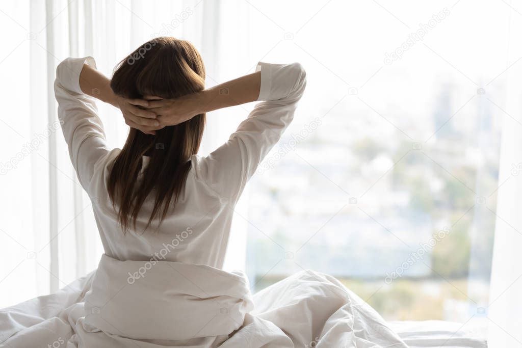 Rear view beautiful woman stretching arms in bed after awakening
