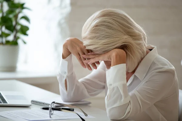 Geschäftsfrau mittleren Alters senkt Kopf über Schreibtisch am Arbeitsplatz fühlt sich ungesund an — Stockfoto
