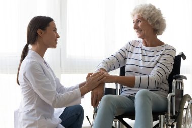 Bakıcı hemşire engelli yaşlı kadını rahatlatıyor tekerlekli sandalyede oturuyor.