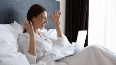 Dizüstü bilgisayar kullanan, yatakta oturan, başarıyı kutlayan heyecanlı bir kadın.