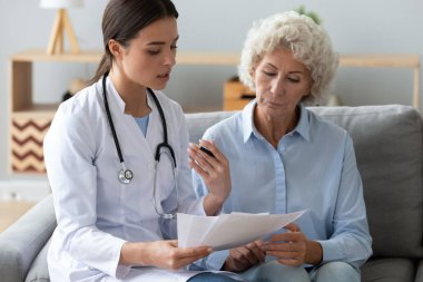 Doktor elinde belgeler tutuyor, yaşlı kadına muayene sonucu hakkında danışmanlık yapıyor.