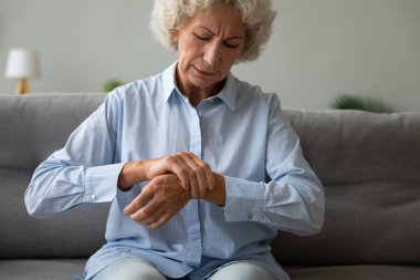 Unhappy older woman massaging wrist, feeling pain in joint clipart