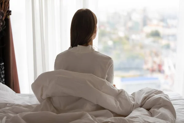 Pandangan belakang wanita muda duduk di tempat tidur setelah terbangun — Stok Foto