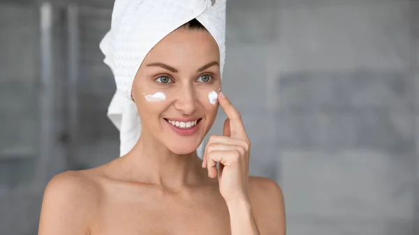 Head shot smiling beautiful woman with perfect skin applying cream