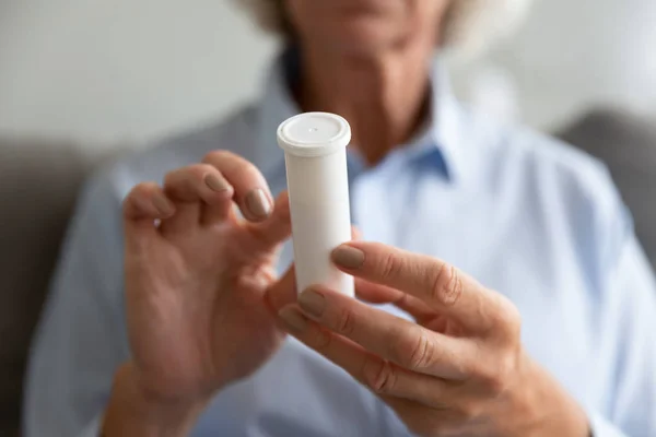 Close up older woman holding white plastic bottle with pills — Stock Photo, Image