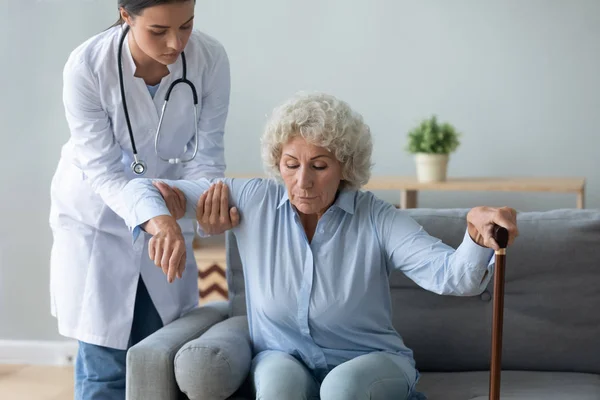 Nurse helping older woman with walking cane to get up