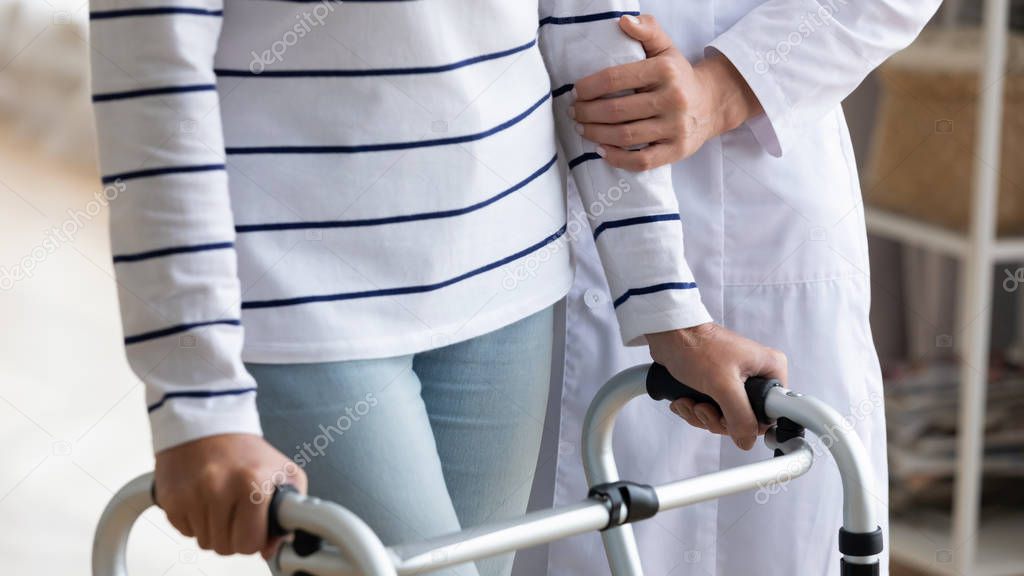Close up nurse helping disabled older woman to use walker