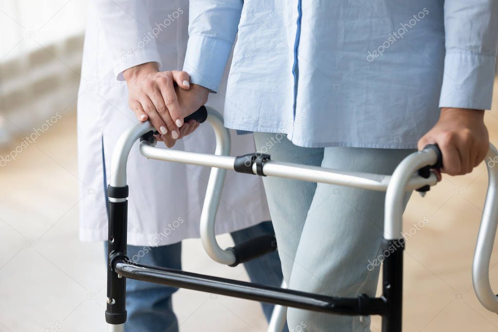 Close up nurse holding disabled older woman hand on walker