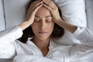 Baş ağrısı çeken depresyondaki kadın yatakta yatıyor.