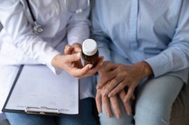 Doktor şişeyi ilaçla kapatıyor, yaşlı hastaya danışıyor.