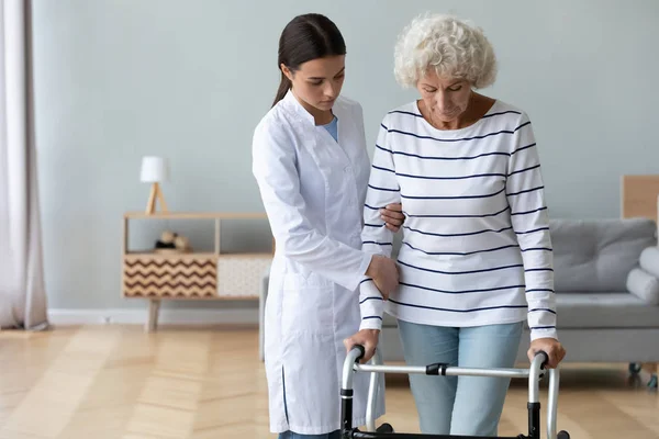 Medico serio che insegna alle donne anziane disabili ad usare walker — Foto Stock