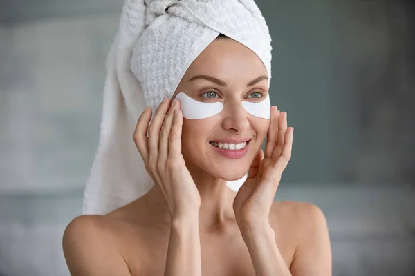 Head shot smiling woman applying hydrogel patches under eyes