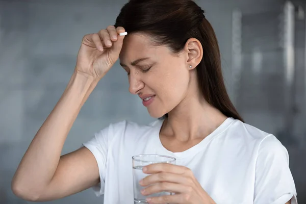 Doente mulher infeliz que sofre de dor de cabeça, segurando pílula, tocando na testa — Fotografia de Stock