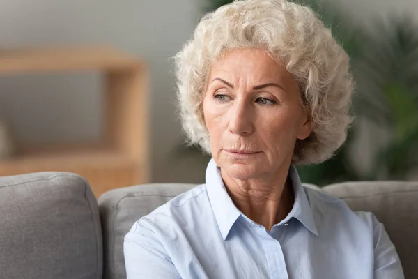 Head shot older woman lost in thoughts, sitting on couch — Stock Photo, Image