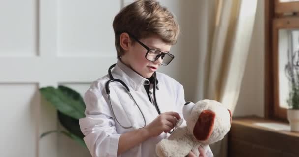 Divertido niño preescolar usar abrigo médico celebrar estetoscopio escuchar juguete — Vídeos de Stock