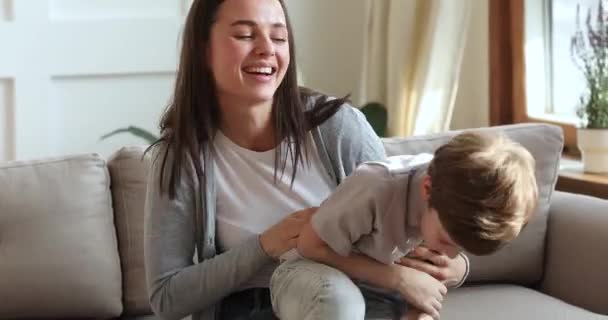 Glückliche Mutter kitzelt niedliches Kind Sohn lacht auf Couch spielen — Stockvideo