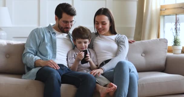 Usmívající se rodiče s dítětem syn relaxovat na pohovce pomocí smartphonu