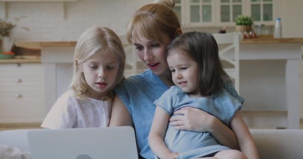 Joven madre abrazando a dos hijas pequeñas, mirando la pantalla del ordenador portátil . — Vídeo de stock