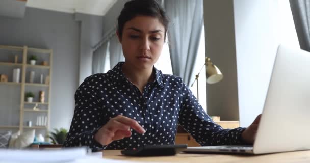 Serious indian woman calculating domestic bills paying online on laptop — Stock Video