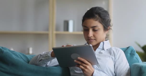 Indian woman relaxing at home on couch using digital tablet — Stock Video