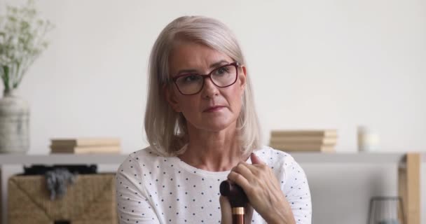 Thoughtful sad old woman holding cane sit alone on sofa — Stock Video