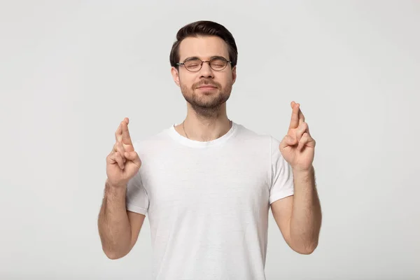 Studio portret millennial guy in bril kruisen vingers. — Stockfoto