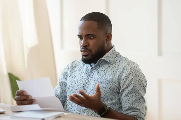 Africano sentado a la mesa sosteniendo carta leyendo noticias horribles — Foto de Stock