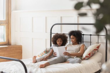 Yatakta uzanmış Afrikalı anne kızına yatmadan önce kitap okuyor.