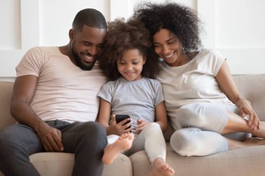 Afrikalı bir aile kanepede oturmuş akıllı telefon uygulamaları kullanarak eğleniyor.