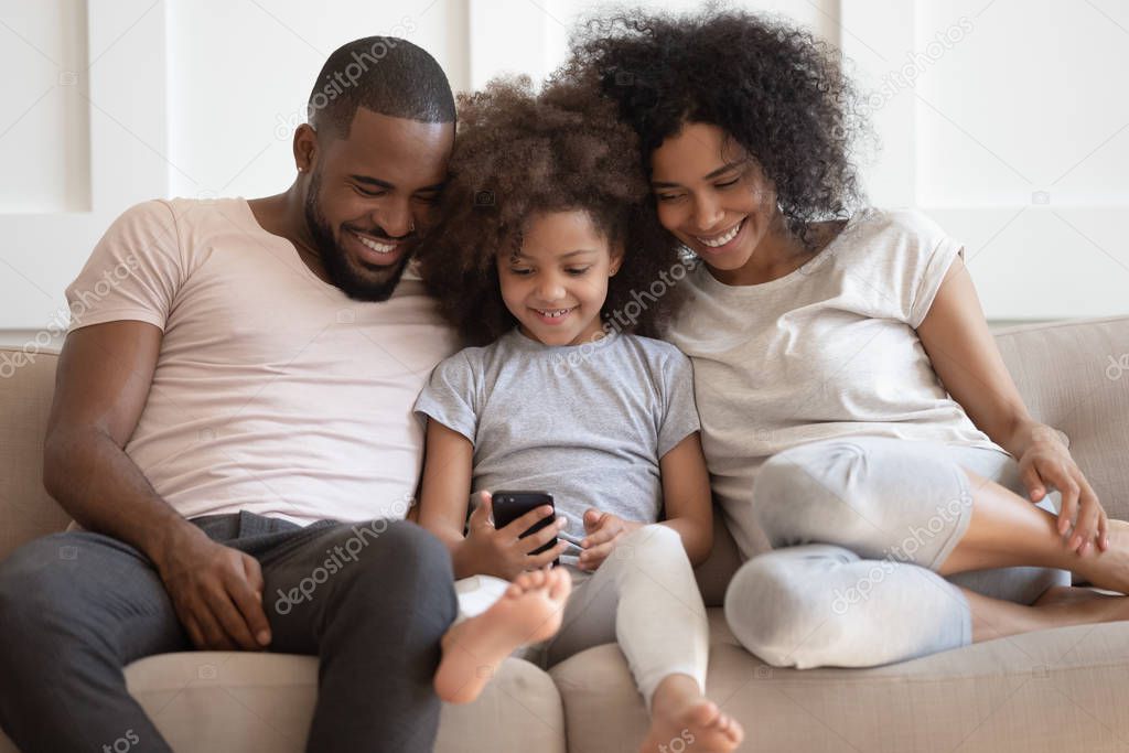 African family sitting on couch having fun using smartphone apps