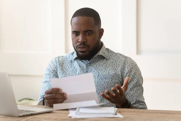 Hombre africano confuso sosteniendo carta de correo leyendo impactantes noticias inesperadas —  Fotos de Stock