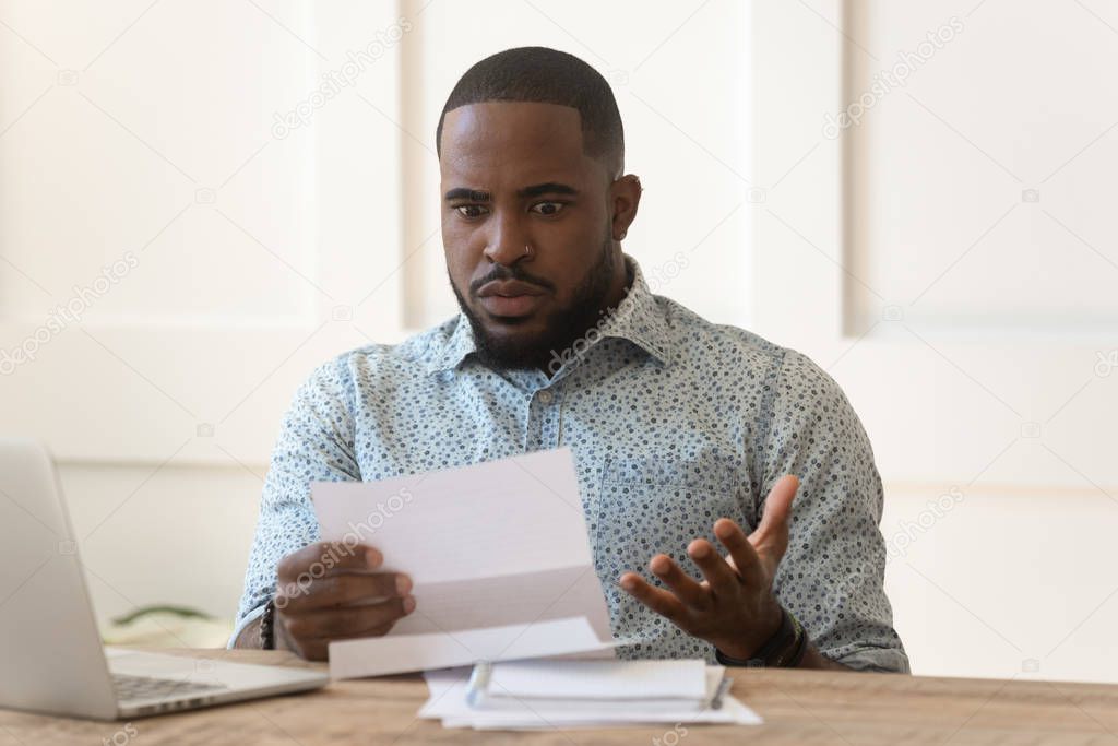 Confused african man holding mail letter reading shocking unexpected news