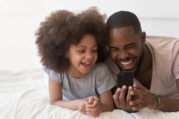 Papa et sa fille couchés au lit s'amusent en utilisant un smartphone — Photo