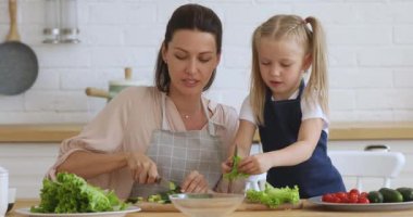 Mutlu 30 'lu yaşlarda bir kadın küçük kızına sağlıklı vejetaryen yemekleri öğretiyor..