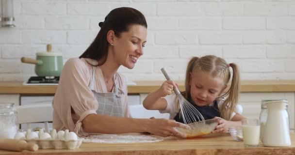 Happy 30s mother watching small preschool daughter whisking egg mass. — Stockvideo
