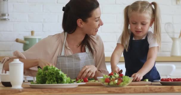 Счастливая мамочка учит маленькую милую дочь резать овощи . — стоковое видео
