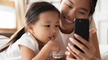 Gülümseyen Vietnamlı anne ve küçük kızı birlikte cep telefonu kullanıyor.