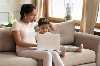 Genç Asyalı anne ve kızı birlikte dizüstü bilgisayar kullanıyorlar.
