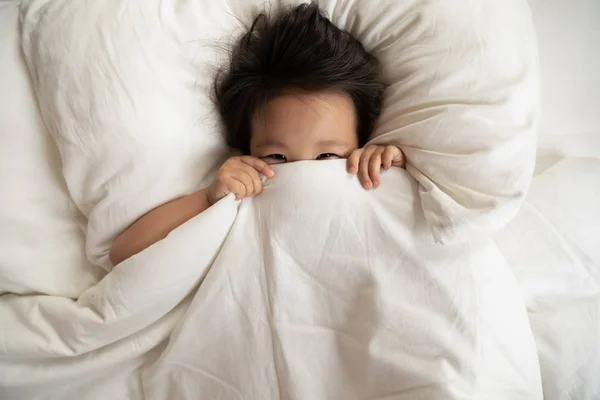 Happy gadis Asia kecil bersembunyi di bawah selimut di tempat tidur — Stok Foto