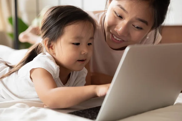 Joven asiática mamá y pequeña hija usando el ordenador portátil en casa —  Fotos de Stock