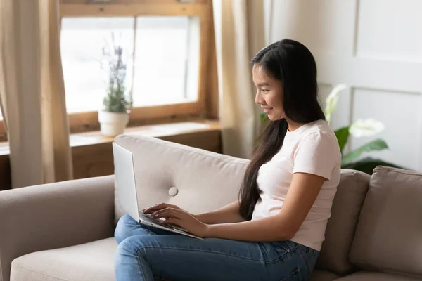 Smiling Vietnamese girl typing on modern laptop at home — Stock Photo, Image
