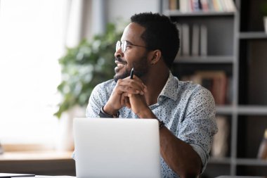 Gülümseyen Afrikalı iş adamı yüzünü çevirmiş laptopla çalışırken hayal kuruyor.