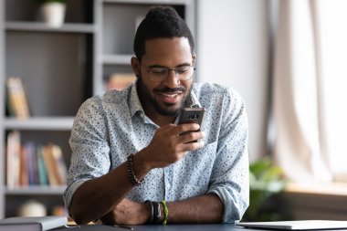 Akıllı telefon kullanan mutlu bir Afrikalı ofis masasında oturuyor.