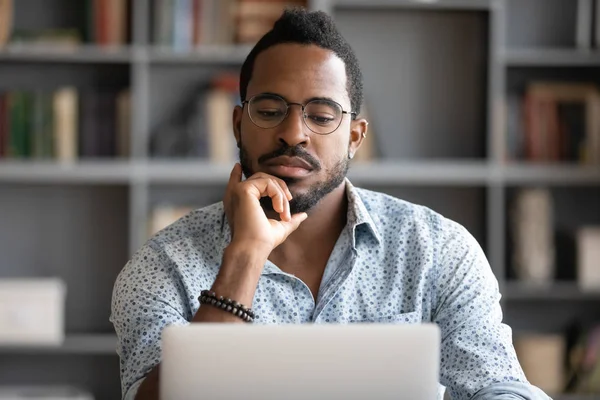 Serious thoughtful african businessman looking at laptop thinking problem solution — Stock Photo, Image