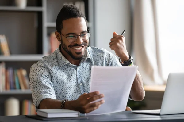 Happy satisfied african male professional read good news in document — Stock Photo, Image
