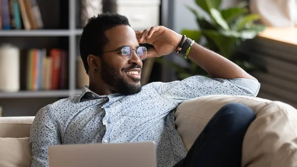 Χαρούμενος Αφροαμερικάνος που χαλαρώνει με το laptop κοιτάζοντας μακριά ονειρεύεται — Φωτογραφία Αρχείου