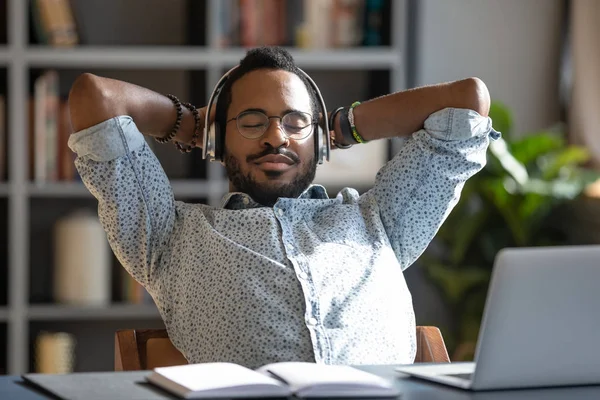 Homem de negócios africano relaxado usa auscultadores a ouvir música na secretária — Fotografia de Stock