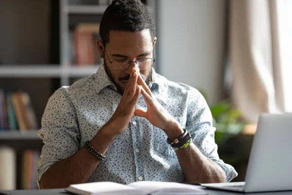 Young african american businessman praying sit at work desk — Stock Photo, Image