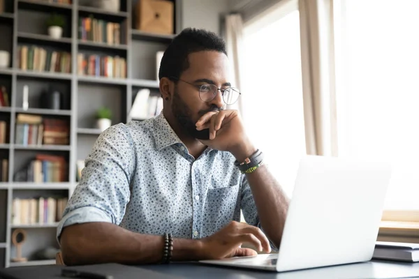 Gericht geconcentreerd Afrikaans zakenman zit achter bureau kijken naar laptop — Stockfoto