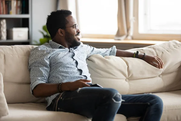 Santai african pria dinginkan di sofa di rumah memegang telepon — Stok Foto